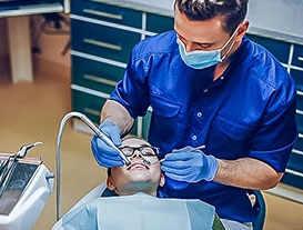 dentist performing a dental cleaning for young child in glasses