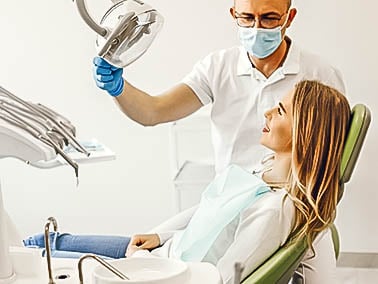 female patient sitting in dental treatment chair with dentist shining procedure light