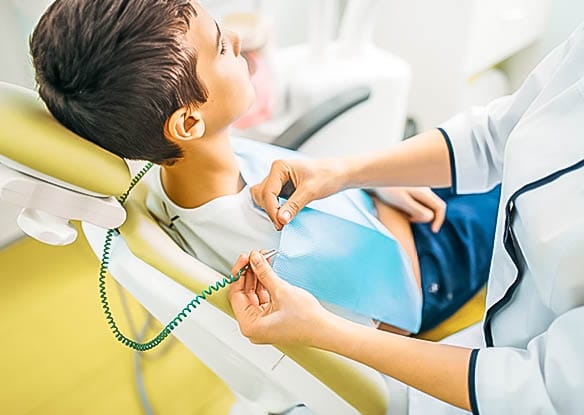 dental hygienist clipping bib to child receiving dental cleaning