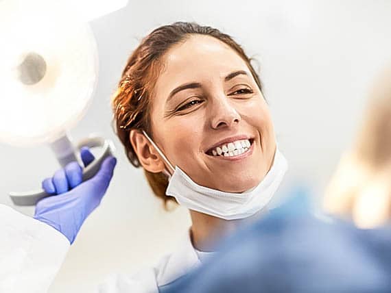 smiling female dentist shining light in dental patients face