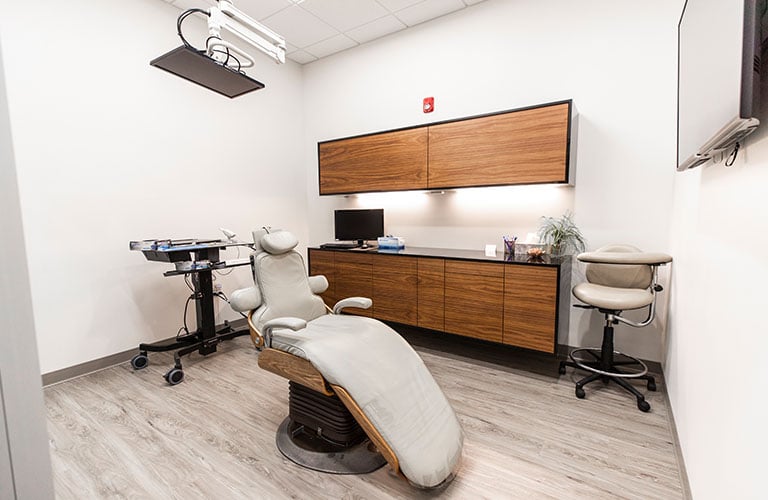 dental treatment room with beige patient chair, light wood floors, and modern cabinets
