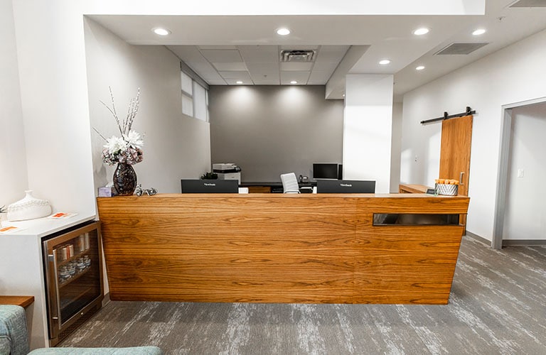 modern wood receptionist desk and beverage fridge in arete smile design waiting room