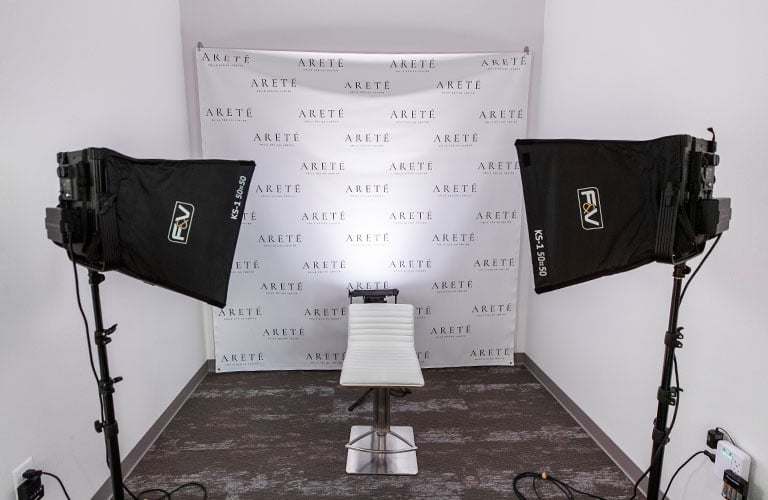 box lights shining on single white chair in front of backdrop with arete logo